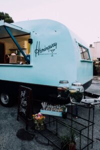 A retro blue food truck in a city street serving beverages with stylish outdoor decor.