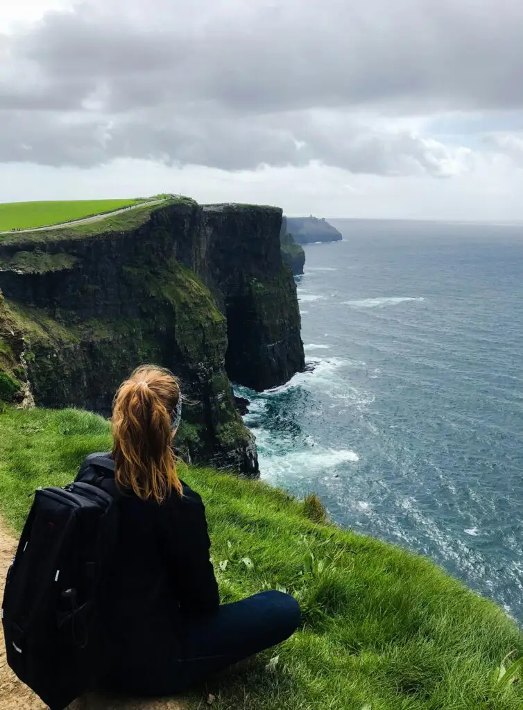 Woman sitting and admiring the stunning Cliffs of Moher in County Clare, Ireland.